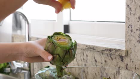 la mujer frota las alcachofas con limón. proceso de cocción en la cocina moderna