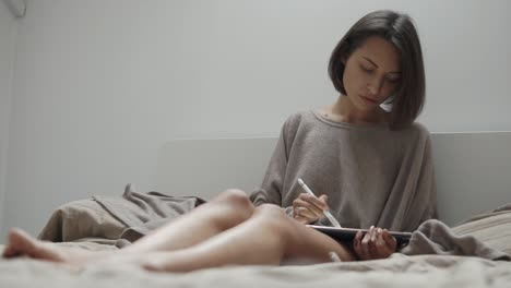 woman drawing on tablet in bed