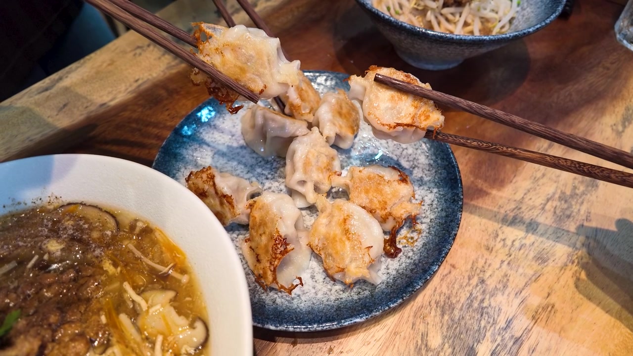 Close-up pangsit goreng renyah di piring biru dengan sumpit mengambil pangsit