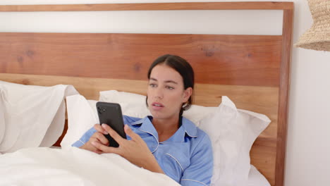 woman in bed using smartphone, wearing pajamas, relaxing in morning, at home