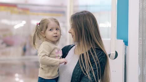 cu slow motion young beautiful mother hugs a little daughter they are in a shopping center smiling