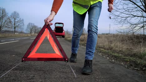 hombre poniendo triángulo de emergencia en la carretera, caminando hacia la cámara