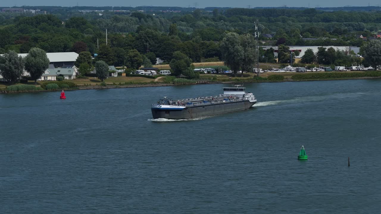 Distant aerial view of loaded Vancouver Barendrecht cargo barge sailing past countryside with buoys, Zuid-Holland, Netherlands