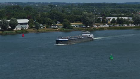 distant aerial view of loaded vancouver barendrecht cargo barge sailing past countryside with buoys, zuid-holland, netherlands