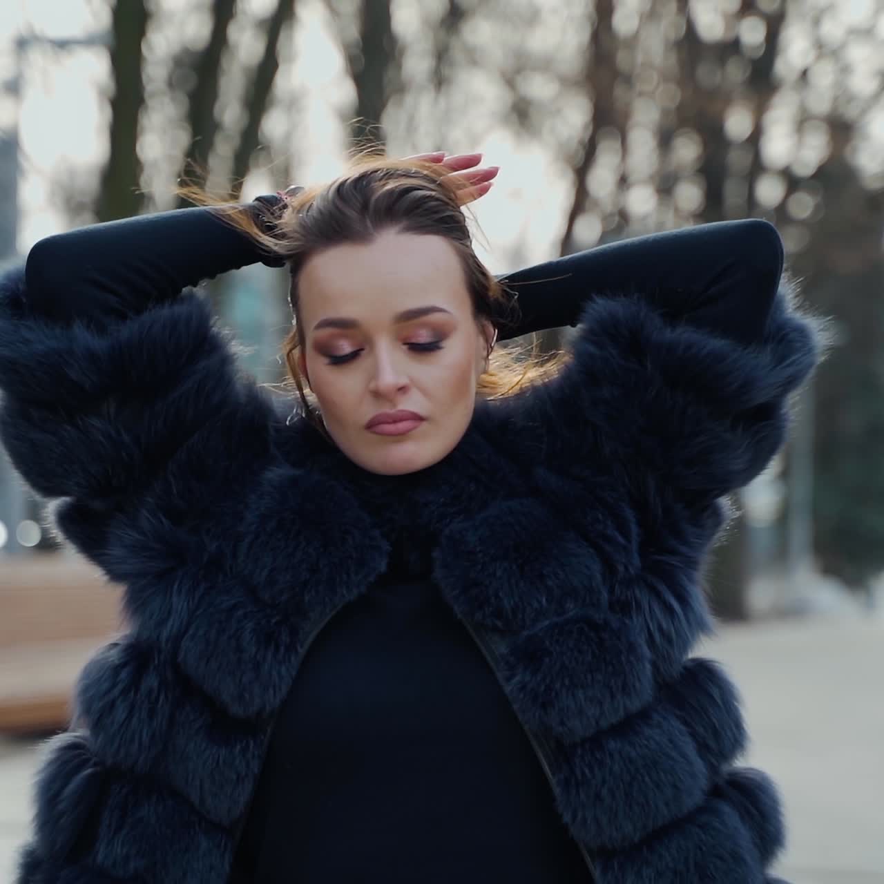 Portrait of a sexy girl outdoors. Attractive woman in a luxury fur coat in the park. Beautiful young model on the city street background. Slow motion.