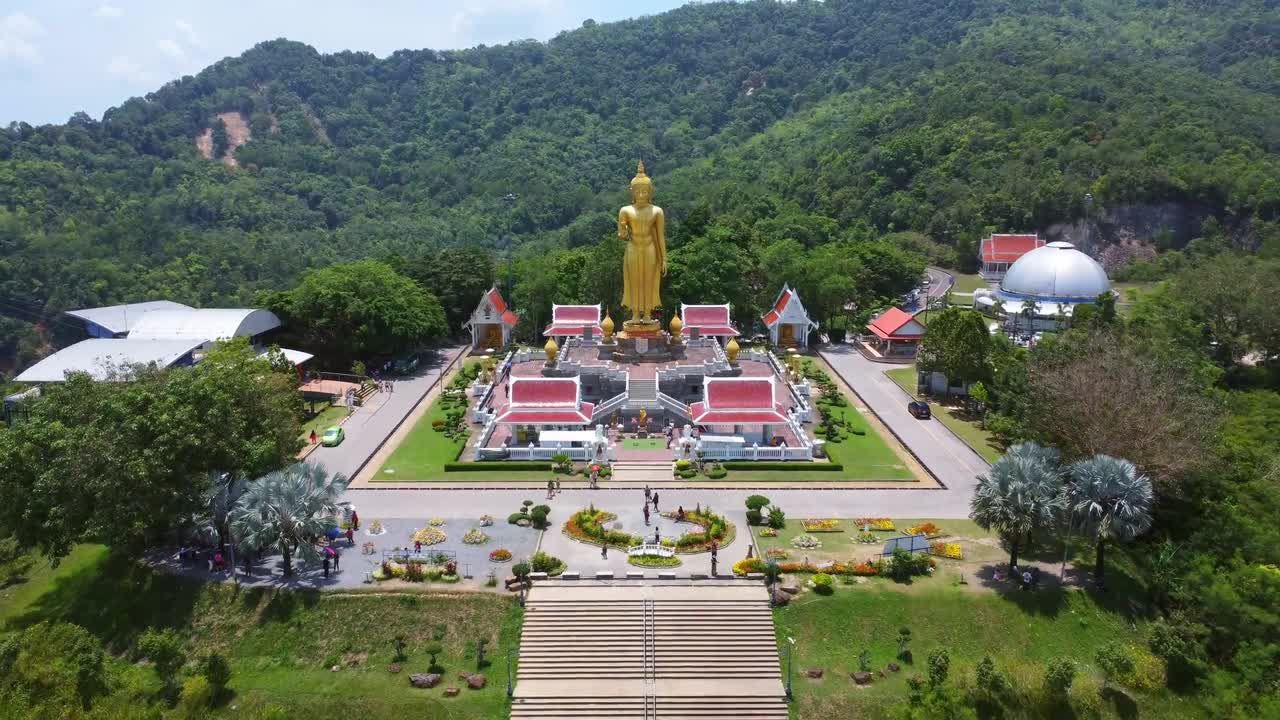 วิดีโอโดรนของพระพุทธรูปทองคำสูงตระหง่านบนแท่นยกพื้น ล้อมรอบด้วยวัดหลังคาสีแดงสดท่ามกลางไหล่เขาแม่ฮ่องสอนที่เต็มไปด้วยป่าเขียวชอุ่ม แสงไฟที่สว่างสดใสช่วยเน้นสีสันที่สดใส
