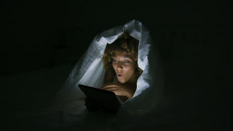 excited woman under blanket with tablet