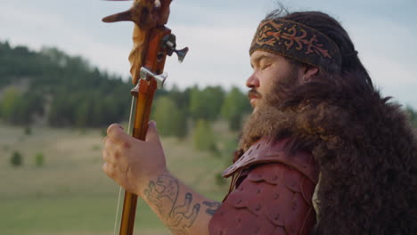 musician with headband and fur holds tovshuur in valley