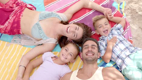 portrait of happy caucasian family lying on towels at beach