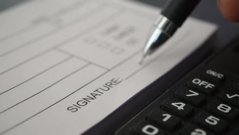 signing a document with a pen and calculator