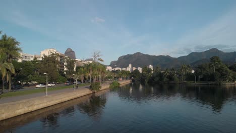 Panorámica-Aérea-Hacia-Atrás-Junto-Al-Lago-De-La-Ciudad-De-Río-De-Janeiro-Con-Gente-Haciendo-Su-Ejercicio-Matutino-Corriendo-Y-Montando-En-Bicicleta