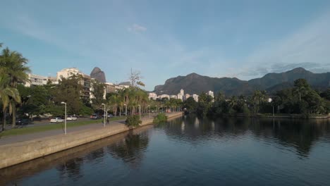 aerial backward panning alongside the city lake of rio de janeiro with people doing their morning exercise running and riding a bicycle