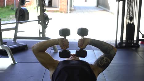 tattoo man muscles in home gym doing dumbbell inward tricep press shot from front