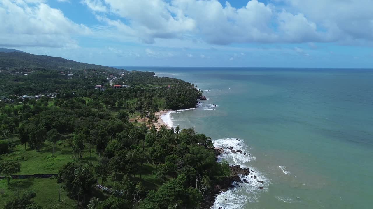 Scenic aerial footage of Koh Lanta, Thailand, showing a remote tropical coastline with lush palm trees, crystal clear turquoise water, rocky shore and hidden beaches in the distance
