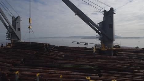 4k drone footage pan of large ship being loaded with logs by cranes