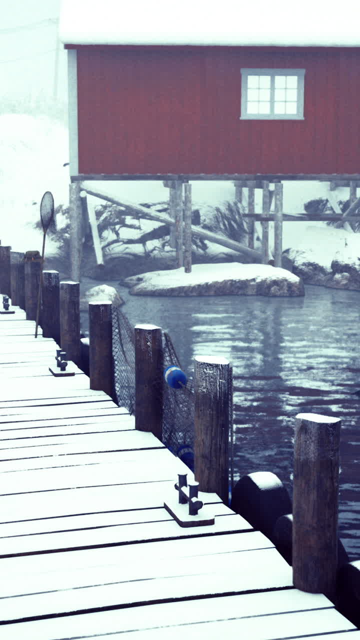 Warm red cabin stands out against snowy winter landscape near water