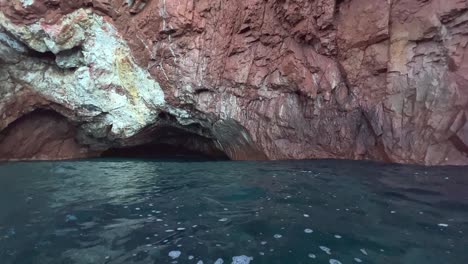 Natural-cave-at-Calanques-de-Piana-seen-from-moving-boat-on-Mediterranean-sea-in-Corsica-in-summer-season,-France