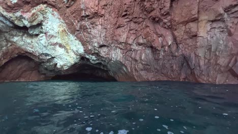 natural cave at calanques de piana seen from moving boat on mediterranean sea in corsica in summer season, france