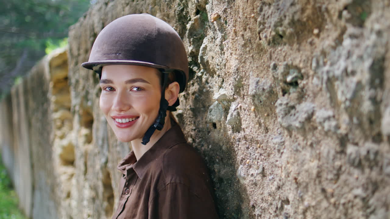 Dreamy horsewoman posing stoned wall portrait. Happy smiling cowgirl in helmet