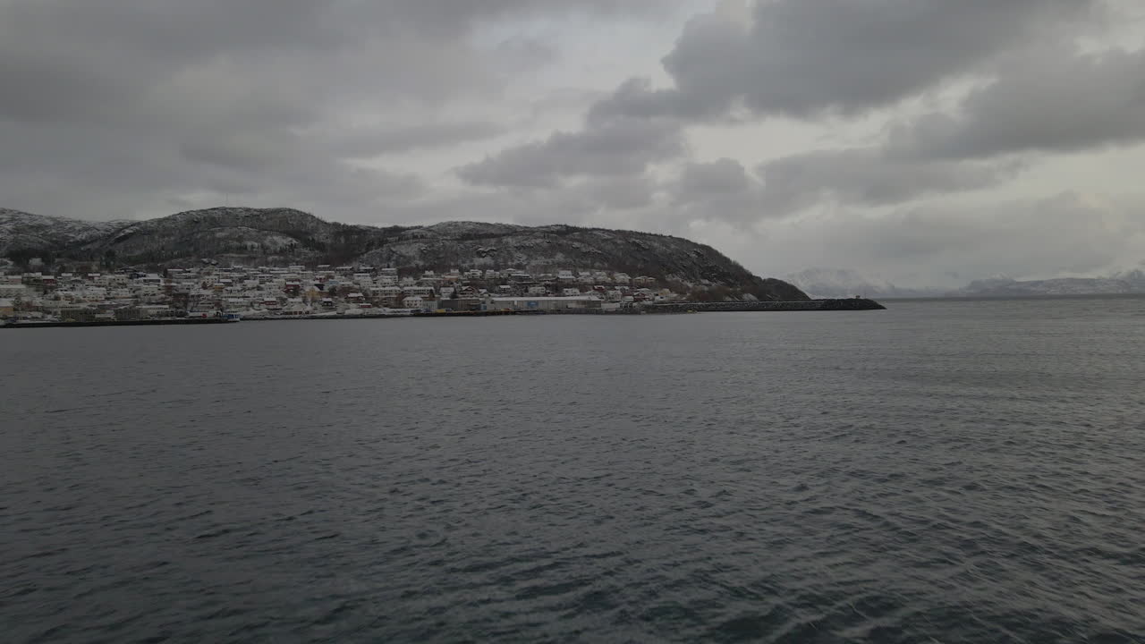 겨울철 흐린 날 노르웨이 트롬스 오그 핀마르크 카운티의 스케르보이 마을을 향해 날아가는 공중 드론 샷