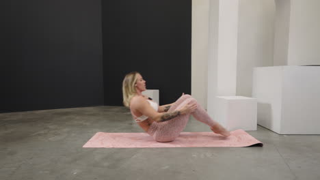 fitness woman instructor performing a core strengthening workout on a pink yoga mat indoors, resting after finishing sets