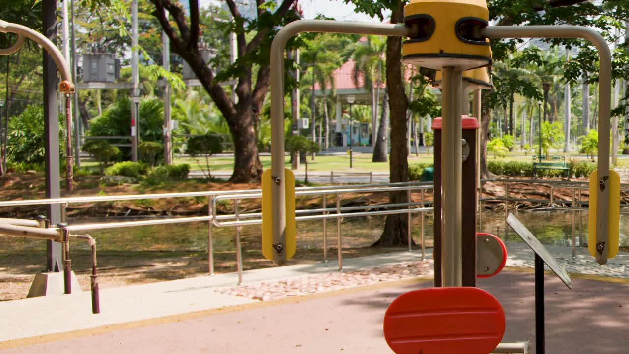 Toma panorámica estática de equipo de fitness vacío en un parque soleado con exuberantes árboles verdes