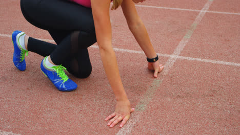 vista lateral de una atleta caucásica tomando la posición de salida en una pista de correr en un lugar deportivo 4k