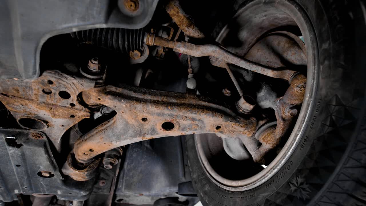 Underneath the rusty front suspension of a used car. Rotating shot with movement in 4k.