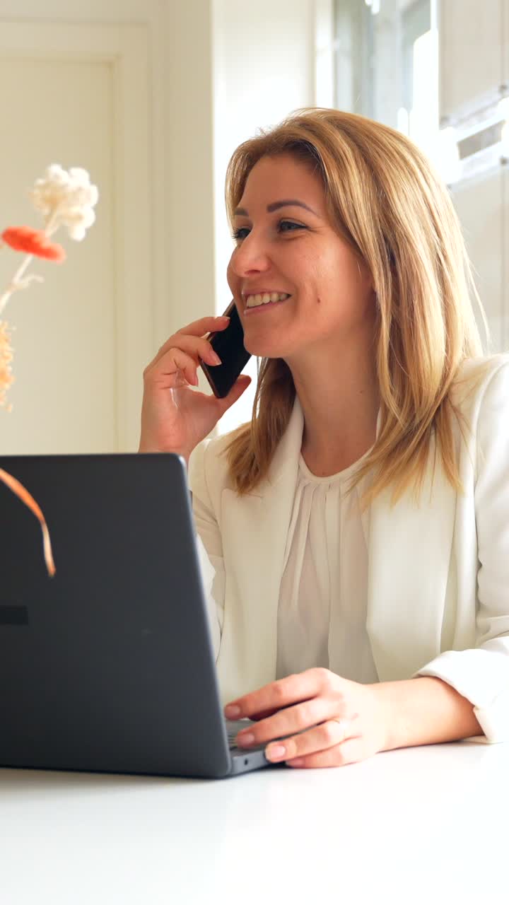 Donna che lavora al computer portatile e parla al telefono