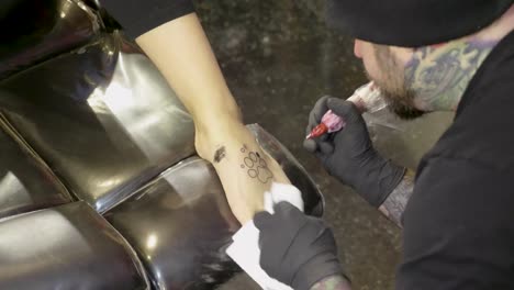 tattoo artist placing small black and white tattoo dog paw on ladies foot cu
