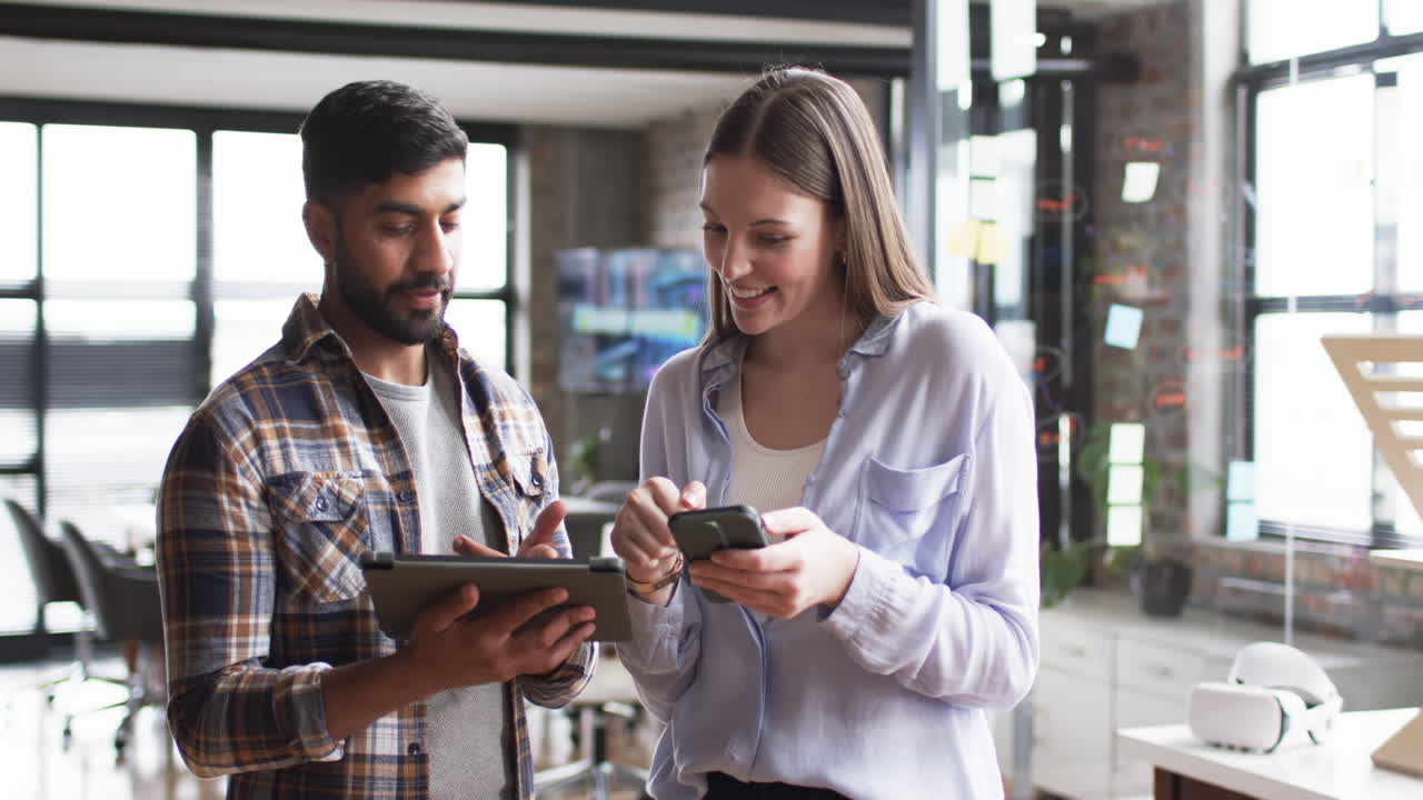 Young Asian man and Caucasian woman review business content on a smartphone in an office setting