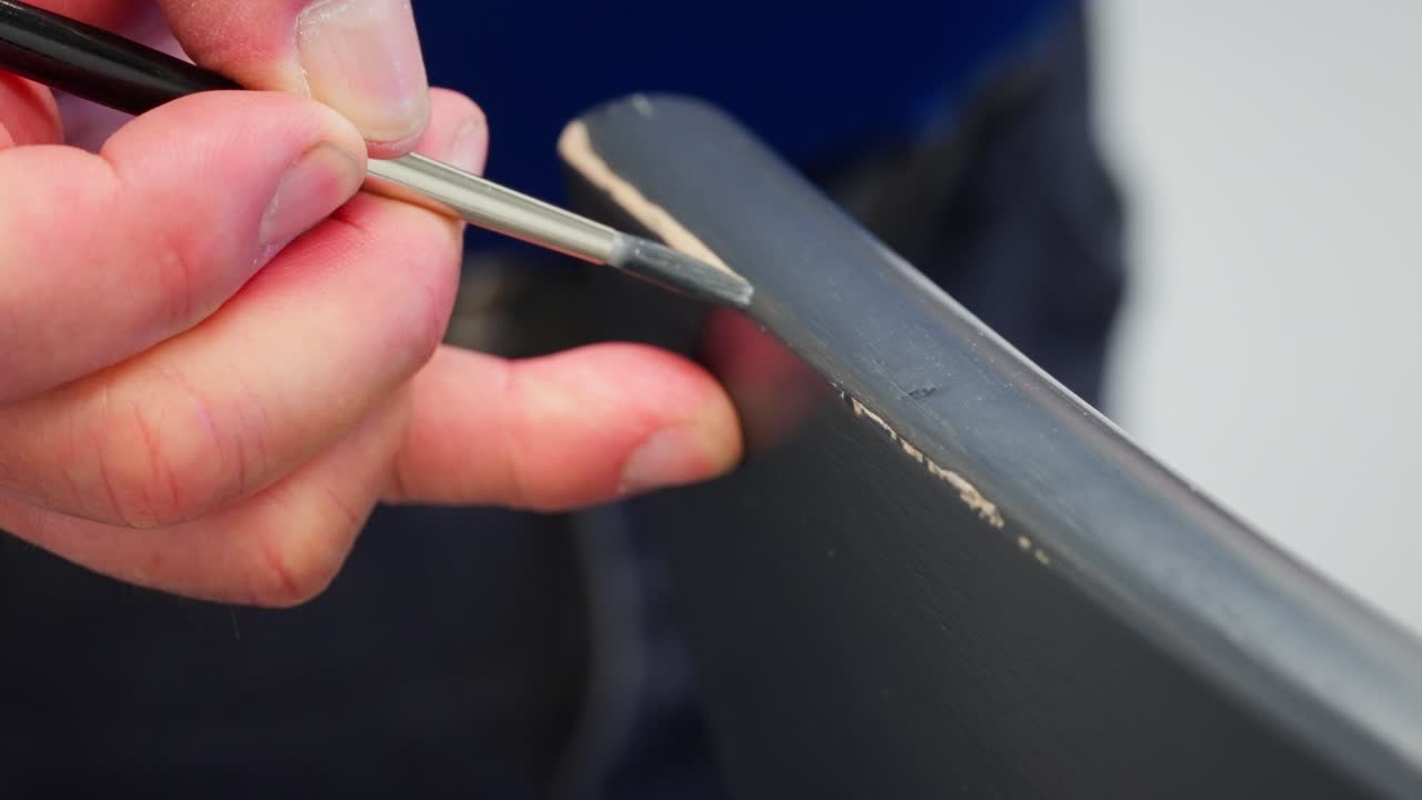 Close up shows man carefully painting grey on chair corner to hide damage