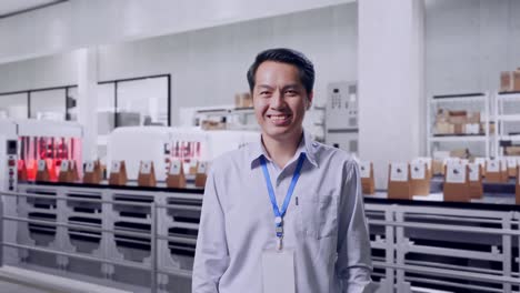 shot captures of an asian male professional worker standing with conveyor for packaging coffee beans in bags at coffee factory, his broad smile at the camera