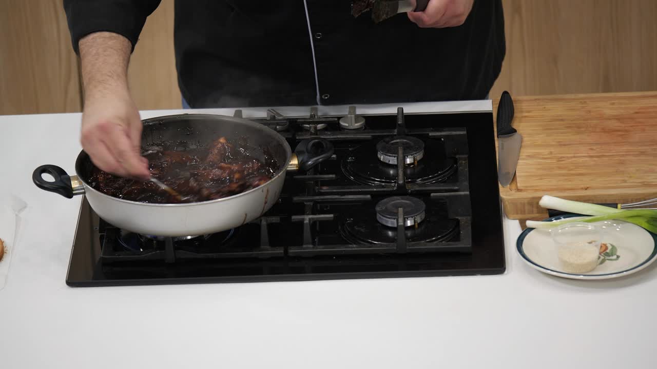 An individual prepares a flavorful beef dish, stirring ingredients in a pan over a gas stove while surrounded by fresh vegetables and kitchen utensils
