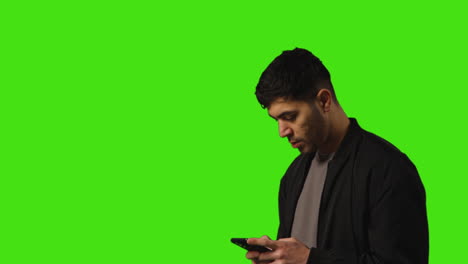 joven entrando en el cuadro de mensajes de texto en el teléfono móvil de pie contra el fondo de la pantalla verde