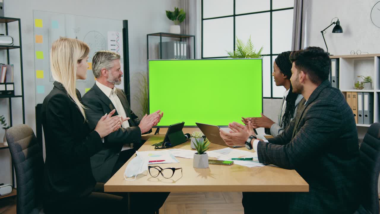 atractivos satisfechos exitosos altamente calificados hombres de negocios de raza mixta aplaudiendo después o antes de la presentación en la pantalla verde de la televisión en una moderna sala de conferencias