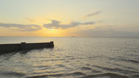 Ship-on-horizon-with-rise-up-and-breakwater-silhouette-during-sunset-in-slow-motion-at-Fleetwood,-Lancashire,-UK