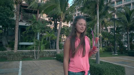 beautiful girl drinks pink cocktail looking away near hotel