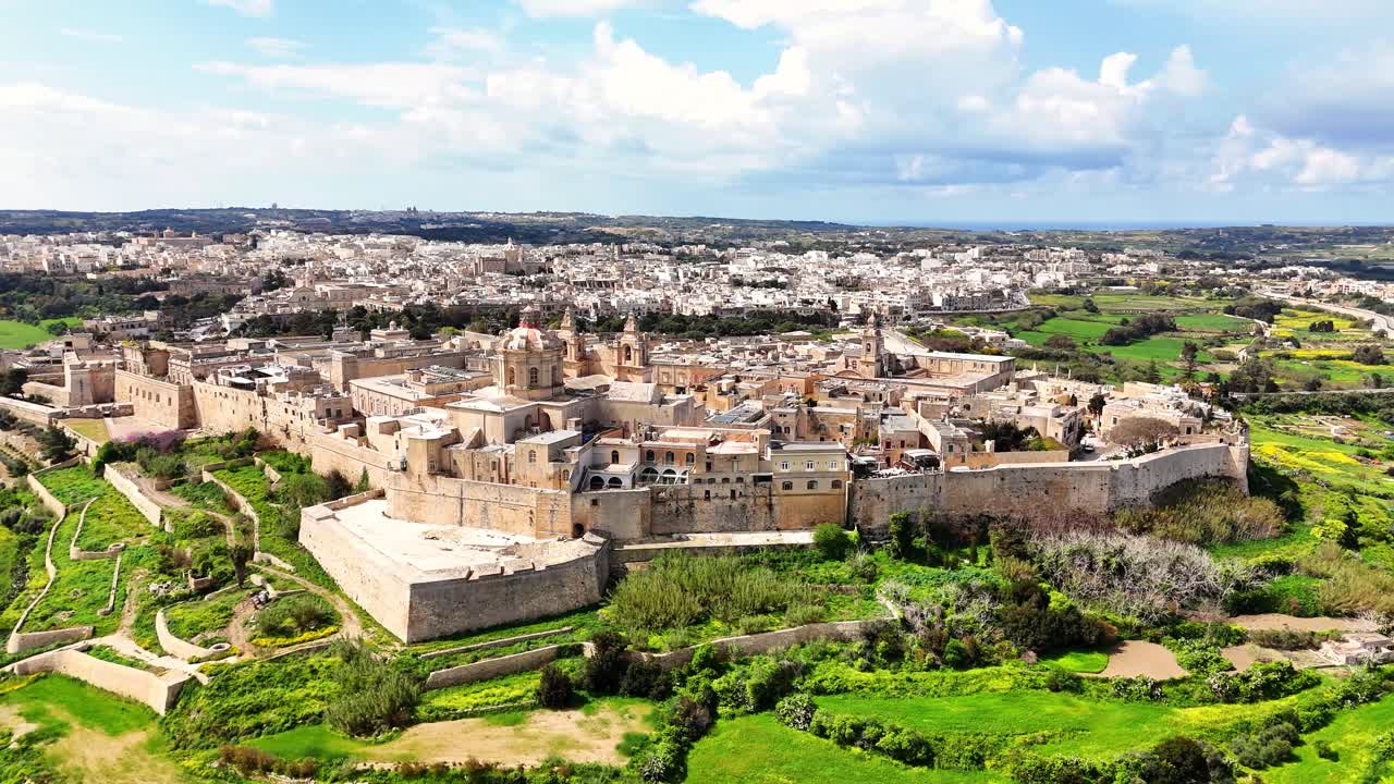 Vista aerea di Mdina a Malta che mostra la città fortificata e murata con la cattedrale, densi edifici in pietra e la campagna verde circostante in pieno giorno.