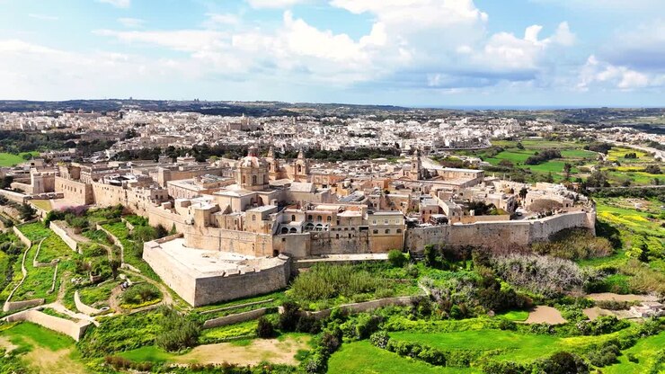 Vista aerea di Mdina a Malta che mostra la città fortificata e murata con la cattedrale, densi edifici in pietra e la campagna verde circostante in pieno giorno.