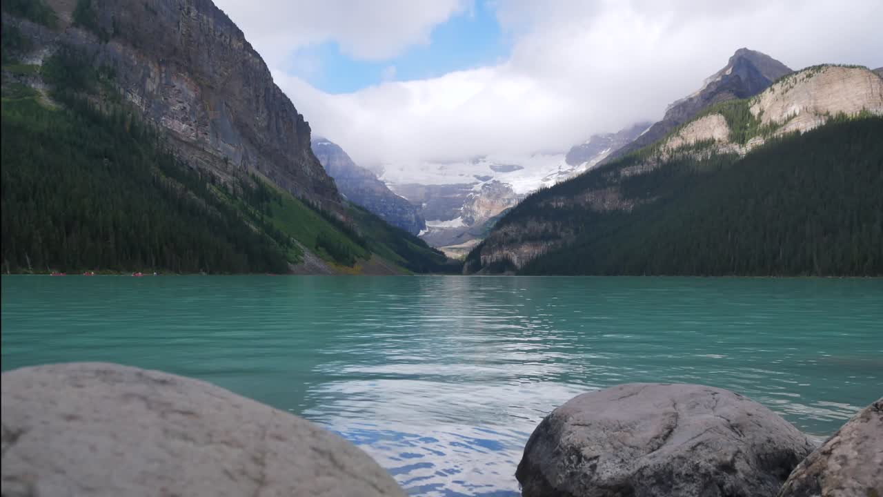 vista panorámica del lago louise, uno de los lagos más famosos del parque nacional de banff, alberta, canadá, en verano durante el día después de llover con nubes en el cielo y gente en canoa en el lago