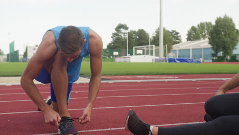 Two-runners-doing-stretch-exercises-on-a-racetrack,-handheld-shot