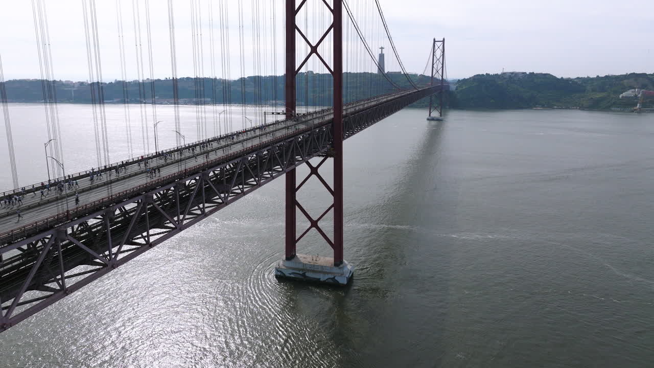 Half marathon and 10K long distance running event in Lisbon, Portugal, Europe. Runners crossing the iconic famous red 25th April suspension bridge by Cristo Rei. Drone rising