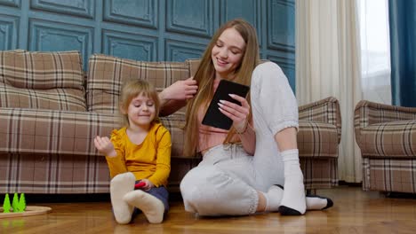 mother and daughter child sit on floor at home working on mobile phone and tablet, watching cartoon