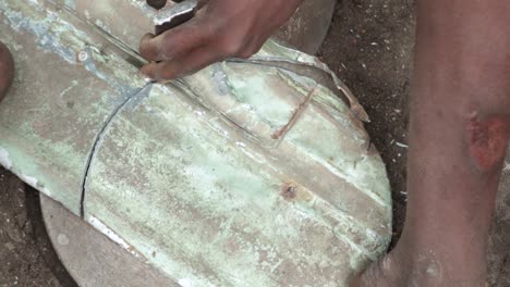 high angle shot of a congolese teenager chiseling a circular metallic sheet for charcoal stove production