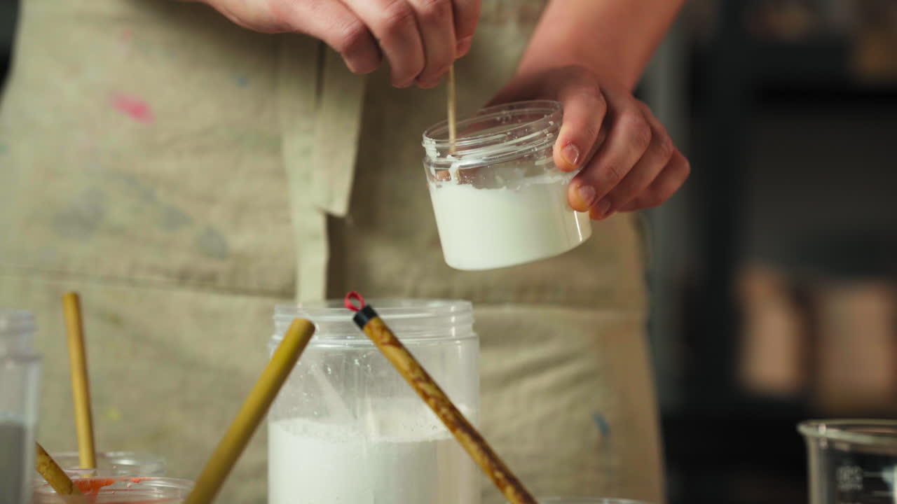 The Person Stirs a Glaze Mixture in a Small Jar, Preparing it For Clay Cup Glazing - Close Up