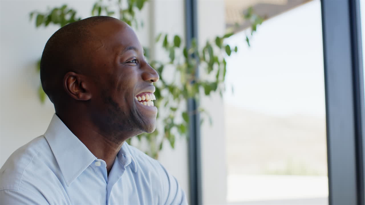 Smiling African American man in office looking out window, enjoying moment of happiness, copy space