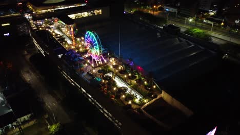 night, aerial and circular view of a shopping center with an amusement park with colored lights on the terrace and people enjoying