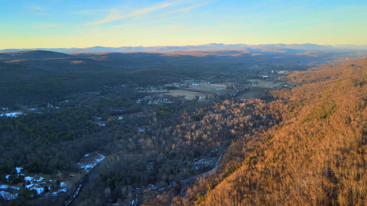 Flying high above a vast valley at sunset, with distant mountains and farmlands and forest during winter