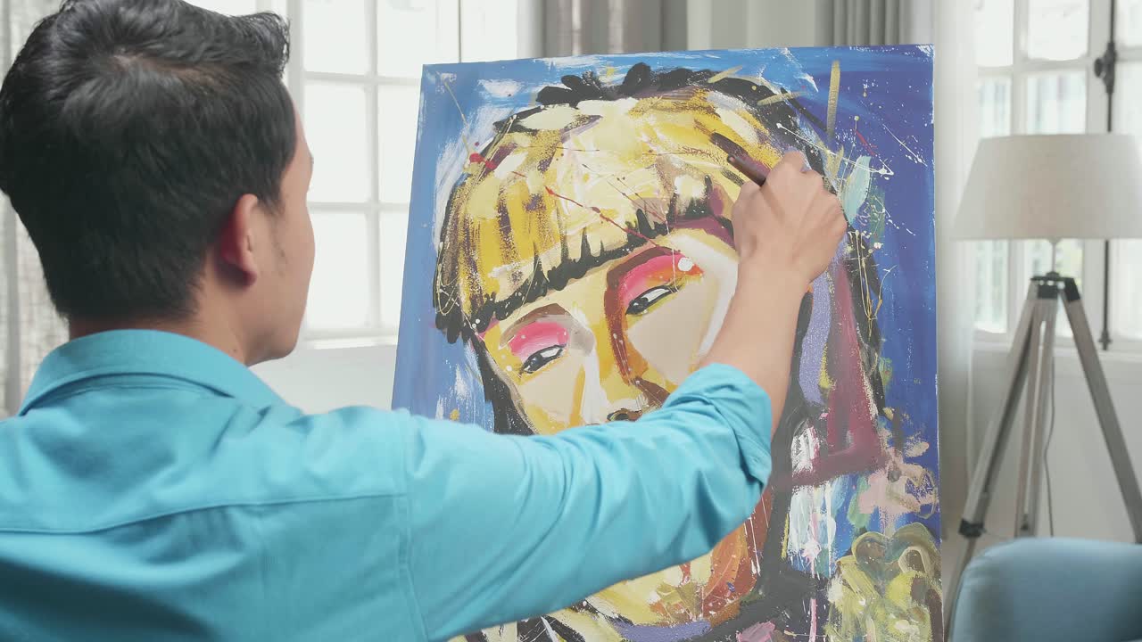 Hind View Of An Asian Artist Man Holding Paintbrush Mixed Colour And Painting A Girl'S Hair On The Canvas